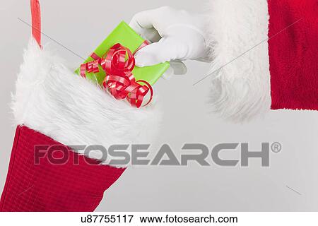 Stock Photo - Santa clause putting gift in Christmas stocking. Fotosearch