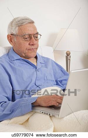 Senior man using laptop, lying in bed View Large Photo Image Picture - Senior man using laptop, lying in bed. Fotosearch