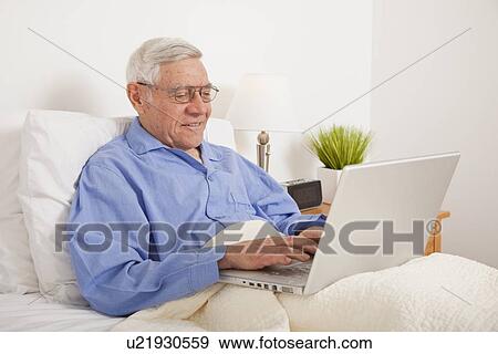 Senior man using laptop, lying in bed View Large Photo Image Stock Photo - Senior man using laptop, lying in bed. Fotosearch