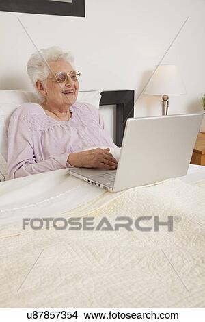 Picture - Senior woman in bed, using laptop. Fotosearch