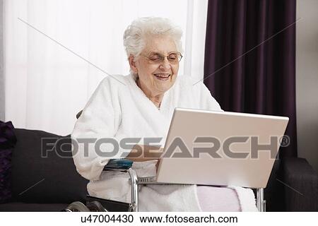 Stock Image - Senior woman on wheelchair using laptop. Fotosearch