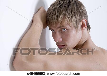 Stock Image - Shirtless young man leaning against wall. Fotosearch