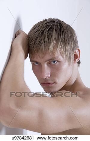 Stock Image - Shirtless young man leaning against wall. Fotosearch