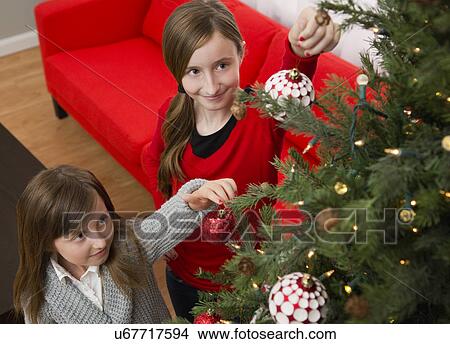 Picture - Sisters (8-9, 10-11) decorating Christmas tree. Fotosearch