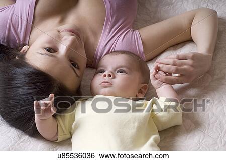 Smiling mother lying with baby (6-11 months) on bed View Large Photo Image Stock Photograph - Smiling mother lying with baby (6-11 months) on bed. Fotosearch