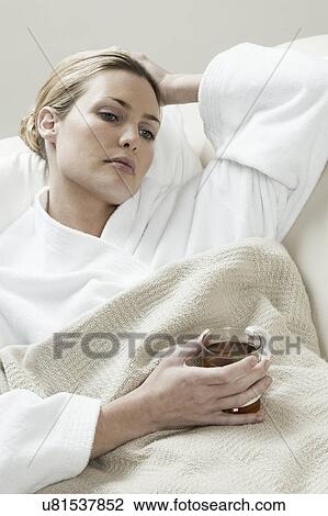 Stock Image - South Africa, Cape Town, Sick young woman lying in bed with tea. Fotosearch