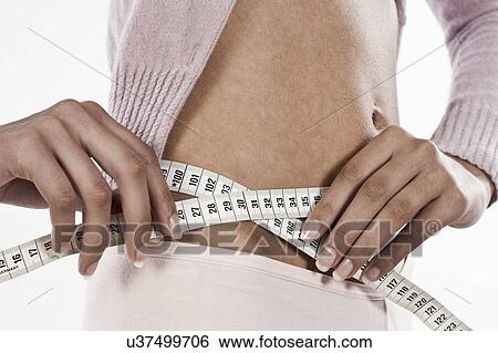 Stock Photograph - South Africa, Cape Town, Young woman measuring waist with tape measure, mid section. Fotosearch