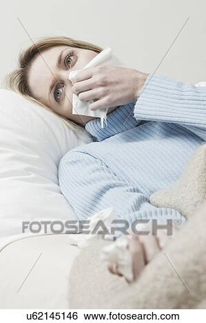 Stock Photograph - South Africa, Cape Town, Young woman lying on sofa and blowing nose. Fotosearch