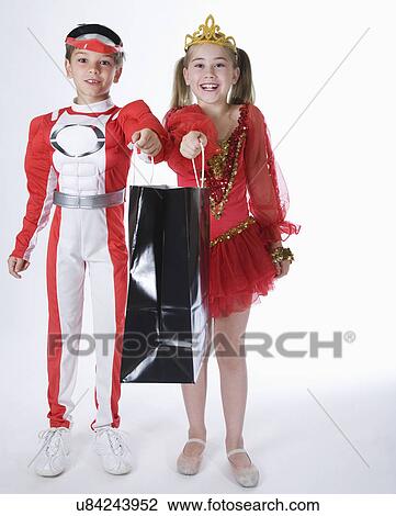 Stock Image - Studio portrait of boy and girl (10-11) wearing costumes and holding gift bag. Fotosearch