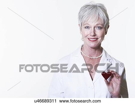 Stock Image - Studio portrait of female doctor holding heart shaped object. Fotosearch