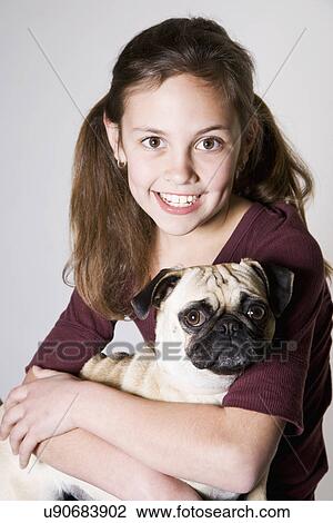 Stock Image - Studio portrait of smiling girl (10-11) holding pug. Fotosearch