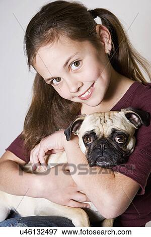 Stock Photo - Studio portrait of smiling girl (10-11) holding pug. Fotosearch