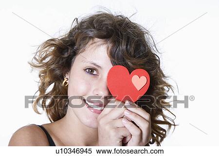 Stock Photography - Studio portrait of smiling teenage girl (14-15) holding heart shaped card. Fotosearch