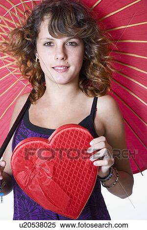 Stock Photography - Studio portrait of smiling teenage girl (14-15) with heart shaped box and umbrella. Fotosearch