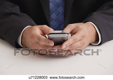Stock Image - Studio shot of businessman text-messaging, midsection. Fotosearch