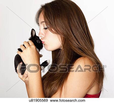 Stock Photo - Studio shot of teenage girl (14-15) kissing small bunny. Fotosearch