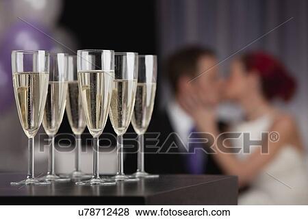 Stock Photo - Table with champagne flutes with couple kissing in background. Fotosearch