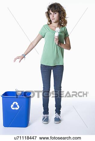 Stock Photo - Teenage girl (14-15) holding environmentally sound lightbulb and throwing traditional light bulb into recycling bin. Fotosearch