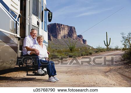 Stock Image - USA, Arizona, senior couple sitting in front of mobile home. Fotosearch