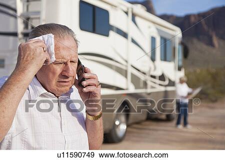Stock Photo - USA, Arizona, senior man standing in front of mobile home talking on mobile phone. Fotosearch