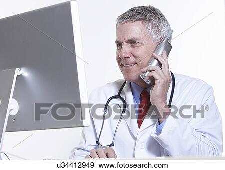 Stock Photo - USA, California, Fairfax, Doctor talking on phone in front of computer. Fotosearch