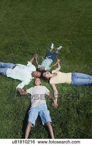 Stock Photograph - USA California, Fairfax, family with two children (6-7, 8-9) lying on grass and holding hands. Fotosearch
