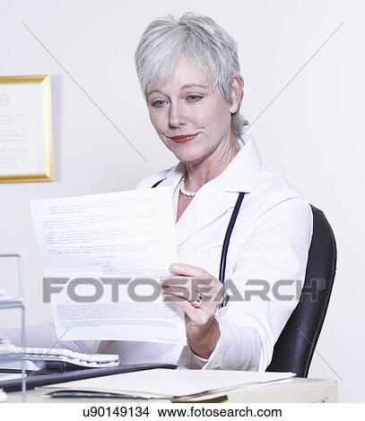 Picture - USA, California, Fairfax, Female doctor reading at desk. Fotosearch