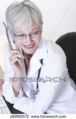 Stock Image - USA, California, Fairfax, Female doctor talking on phone at desk. Fotosearch