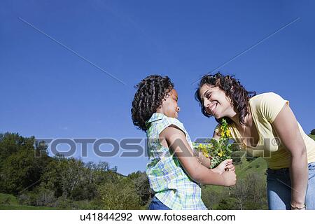 Stock Image - USA California, Fairfax, girl (6-7) giving flowers to mother outdoors. Fotosearch