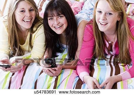 Stock Image - USA, California, Fairfax, girls (15-18) text messaging on bed. Fotosearch