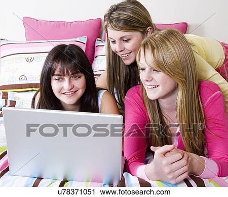 Stock Image - USA, California, Fairfax, girls (15-18) using laptop on bed. Fotosearch