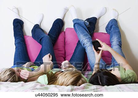 Stock Photography - USA, California, Fairfax, girls (15-18) text messaging on bed. Fotosearch