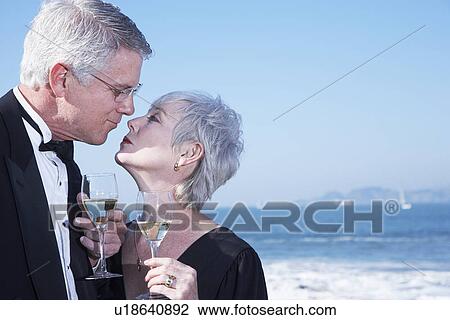 Stock Image - USA, California, Fairfax, Happy mature couple drinking wine and kissing on beach. Fotosearch