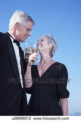 Stock Image - USA, California, Fairfax, Happy mature couple drinking wine on beach. Fotosearch