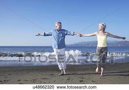 Stock Image - USA, California, Fairfax, Happy mature couple dancing on beach. Fotosearch