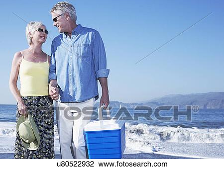 Stock Image - USA, California, Fairfax, Happy mature couple standing on beach. Fotosearch