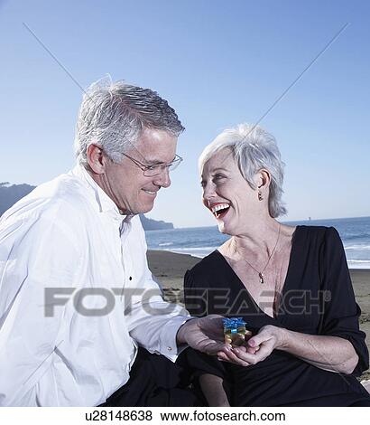 Stock Photo - USA, California, Fairfax, Happy mature mag giving small gift to woman on beach. Fotosearch