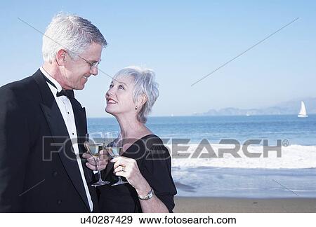 Stock Photo - USA, California, Fairfax, Happy mature couple drinking wine on beach. Fotosearch