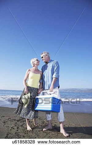 Stock Photo - USA, California, Fairfax, Happy mature couple standing on beach with cooler. Fotosearch