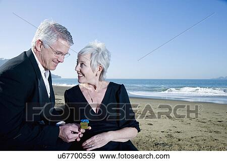 Stock Photo - USA, California, Fairfax, Happy mature mag giving small gift to woman on beach. Fotosearch