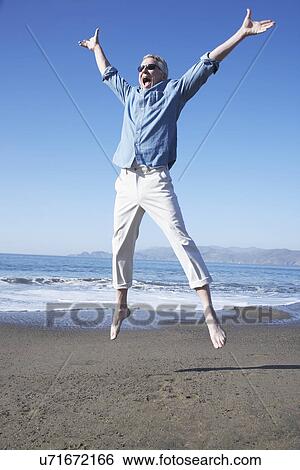 Stock Photograph - USA, California, Fairfax, Happy mature man jumping on beach. Fotosearch