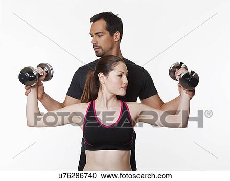 Stock Image - USA, California, Fairfax, Instructor assisting woman lifting handweights. Fotosearch