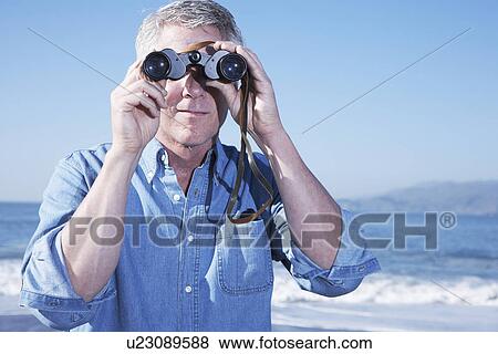 Stock Photo - USA, California, Fairfax, Mature man looking through binoculars on beach. Fotosearch