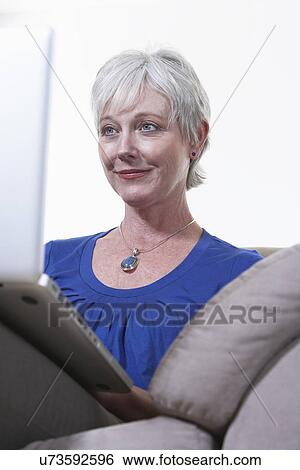Stock Photograph - USA, California, Fairfax, Mature woman sitting on sofa with laptop. Fotosearch