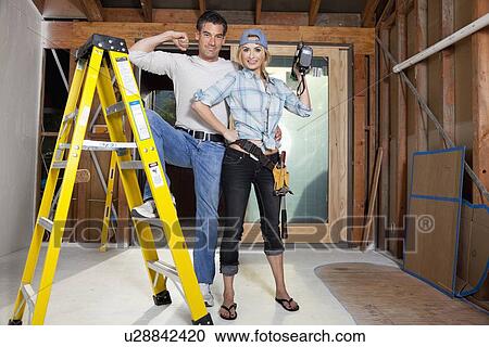 Stock Image - USA, California, Fairfax, Mid adult couple posing with drill and ladder during home improvement work. Fotosearch