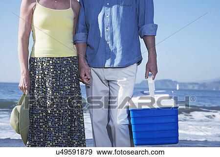 Stock Photo - USA, California, Fairfax, Mid section of mature couple walking on beach with cooler. Fotosearch