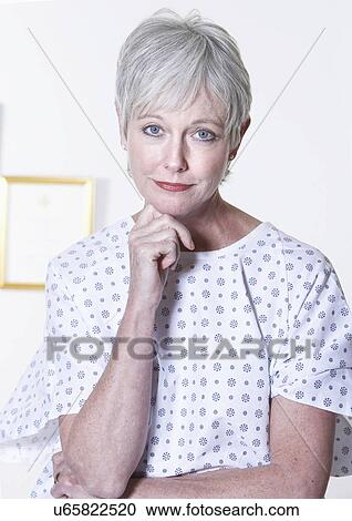 Stock Image - USA, California, Fairfax, Portrait of woman in hospital gown sitting in doctor's office. Fotosearch