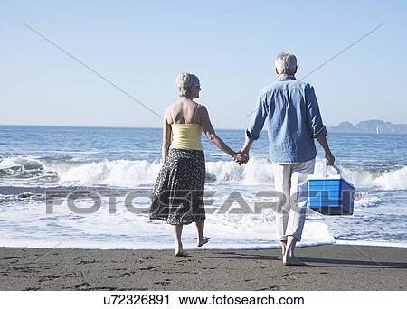 Stock Image - USA, California, Fairfax, Rear view of mature couple walking on beach. Fotosearch