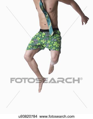 Picture - USA California, Fairfax, studio shot of young man wearing green boxer shorts with shamrocks jumping, low section. Fotosearch