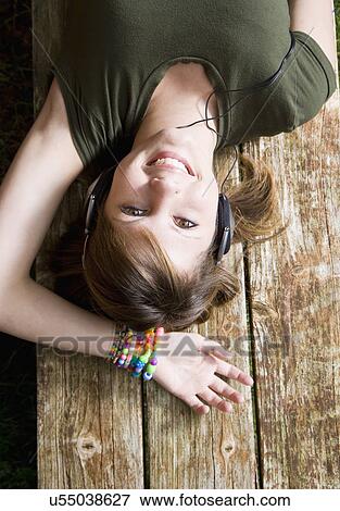 Stock Photo - USA California, Fairfax, teenage girl (16-17) lying on wooden bench and listening music. Fotosearch